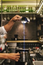 A professional bartender expertly pours a flaming cocktail from a shaker in a stylish bar,