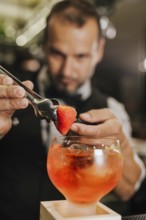 A skilled bartender adds a strawberry garnish to a vibrant cocktail, showcasing his expertise in