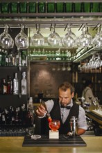 A professional bartender skillfully prepares a vibrant cocktail at an elegant urban bar, surrounded