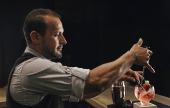 A skilled bartender expertly prepares a colorful cocktail at a lively bar, showcasing precision and