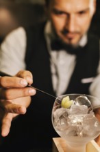 A professional bartender skillfully prepares a cocktail at an elegant bar. Focused on garnishing,