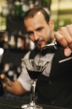 A professional bartender skillfully pours a dark liquid into a martini glass amidst an elegant
