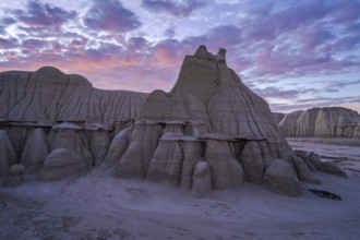 Sunset casts a soft glow over the dramatic and weathered sandstone formations of the