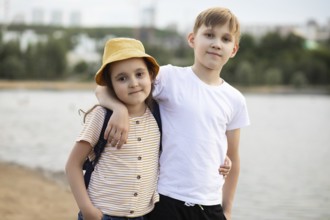 A young brother and sister share a warm moment by a lake. The boy, in a white shirt, lovingly puts