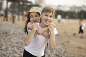 Two joyful siblings, a boy and a girl, share a playful moment outdoors. The girl gives a piggyback
