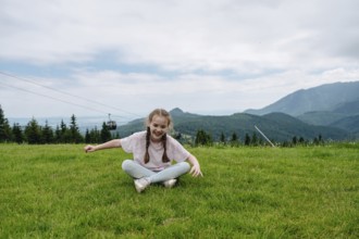Young girl in casual attire, laughing as she sits on lush green grass at Bachledka Ski Sun in