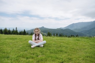 Young girl resting on a grassy hill with a stunning view of the Belianske Tatras, seen from