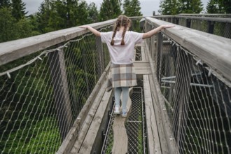 Back view of an unrecognizable girl walking on a treetop bridge at Bachledka. She displays a sense