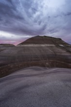 The photo captures dramatic skies at dusk above the layered bentonite hills near Hanksville, Utah,