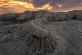 A dramatic sunset illuminates the layered rock formations at Bisti/De-Na-Zin Wilderness in New
