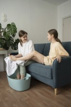 A mother and daughter enjoy a self-care routine at home, bonding over a relaxing foot bath. They