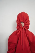 A child wears a red hoodie with the hood pulled tight, completely hiding their face. The