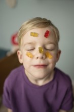 A child with closed eyes smiles blissfully with colorful gummy bears on their face, expressing a