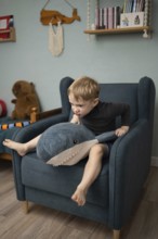 A child sits on an armchair, energetically interacting with a plush shark toy. The cozy room