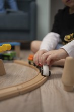 A child sits on the floor, immersed in playing with a wooden train set. The soft focus emphasizes