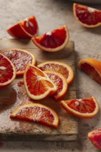 Slices of vibrant blood oranges arranged on a weathered wooden board. The rich red hues and