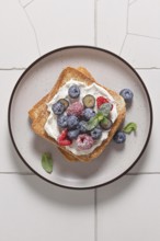 Top view of a delicious toast topped with cream cheese, raspberries, blueberries, and a sprinkle of