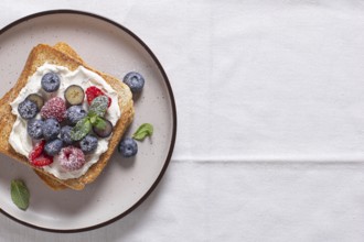 Top view of a delicious toast topped with cream cheese and garnished with raspberries, blueberries,