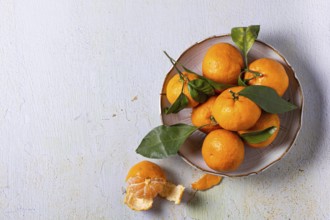 A bowl of fresh tangerines with green leaves, arranged on a textured surface. One tangerine is