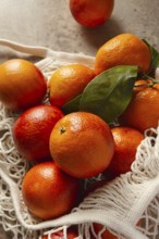 A bunch of vibrant blood oranges with deep red hues sit in a reusable cotton bag on a rustic table.