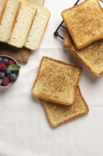 Top view of golden toasts alongside a bowl of blueberries and raspberries on a rustic wooden board