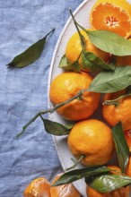 Fresh tangerines with vibrant green leaves are artfully arranged on a textured blue fabric,