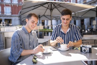 A gay couple enjoys a sunny day while having coffee at a cafe on the streets of Madrid. The scene