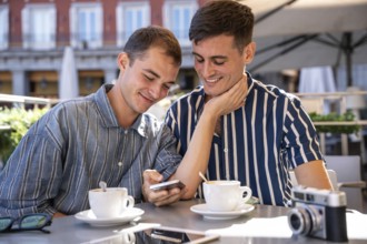 A gay couple shares a joyful moment at an outdoor cafe in Madrid. They smile while looking at a