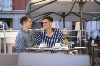 A gay couple shares a joyful moment at a charming outdoor cafe on the streets of Madrid. They are