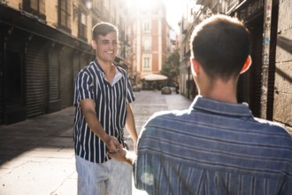 A joyful gay couple holds hands while strolling through the charming sunlit streets of Madrid.