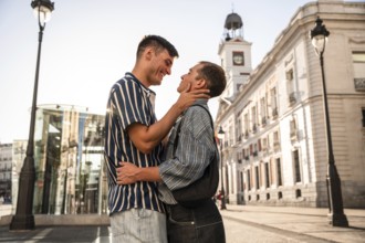 A gay couple shares a tender moment on the vibrant streets of Madrid. The sunlight enhances their