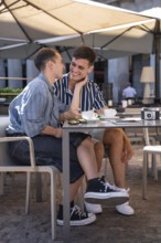 A gay couple shares a joyful moment over coffee at an outdoor cafe in the vibrant streets of
