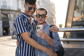 A gay couple embraces and takes a selfie on the streets of Madrid. They are both smiling, enjoying