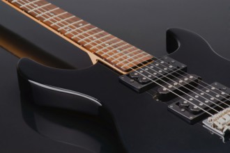 Close up shot of a sleek black electric guitar highlighting its glossy black body and warm wood