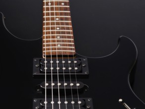 A detailed close up of a sleek black electric guitar with a wooden fretboard and shiny metal