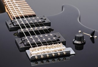 Close up shot of an electric guitar showcasing its strings, pickups, and volume knob. The guitar