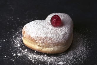 A delectable heart shaped cream bun generously sprinkled with icing sugar and adorned with a glossy