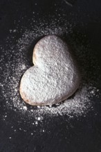 Top view of a delicious heart shaped cream bun generously dusted with icing sugar, presented on a