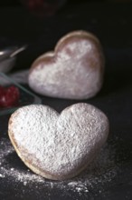 Delicious heart shaped cream buns generously sprinkled with icing sugar, presented on a dark