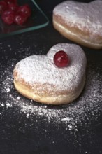 Two heart shaped cream buns, generously dusted with icing sugar and topped with a bright red