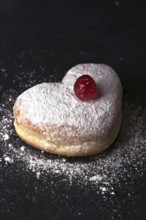 A heart shaped cream bun generously dusted with icing sugar, topped with a vibrant red cherry,