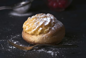 A delectable cream bun sprinkled generously with icing sugar, sitting beside a vintage fork on a