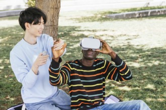 Two friends enjoying virtual reality gaming outdoors. One person wears a VR headset while the other