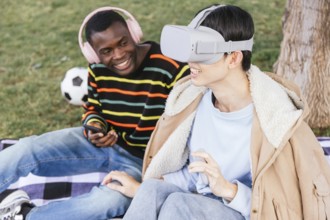 Two friends enjoy a sunny day at the park, one wearing a virtual reality headset, while the other