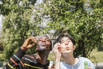 Two friends enjoy a sunny day outdoors, joyfully blowing bubbles. The background features lush