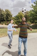 Two friends enjoy a sunny day playing soccer in a park. One balances the ball on his head while