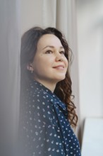 A woman in a patterned blue shirt gazes thoughtfully upward, bathed in soft natural light, creating
