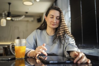 A serene middle-aged woman interacts with a tablet at a sunlit cafe table, amidst a relaxed setting