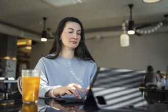 Mid-aged woman browses a tablet at a cafe, staying connected while drinking a glass of orange juice