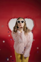 A charming woman with long hair wearing heart-shaped sunglasses and a frilly pink blouse sends a